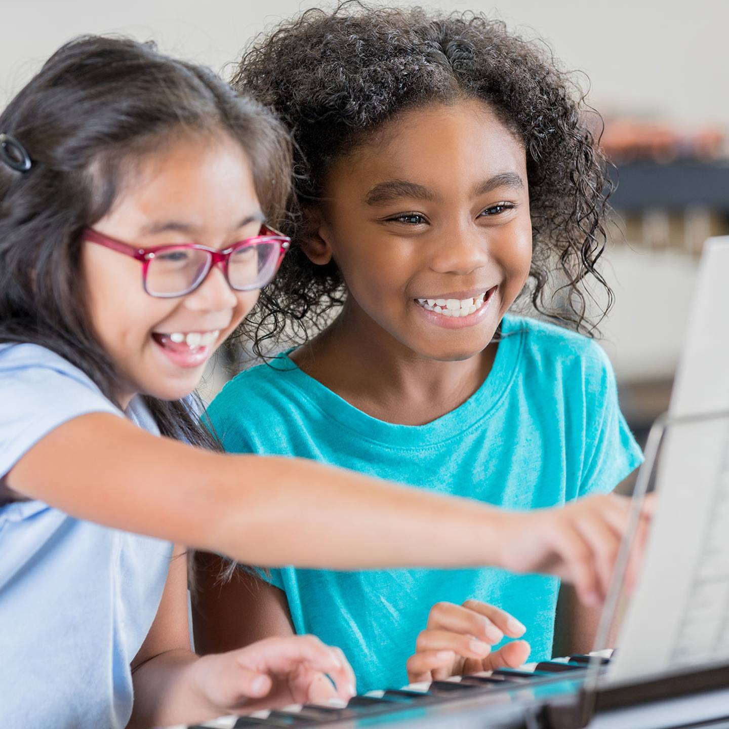 Two children sitting at a piano reading sheet music.